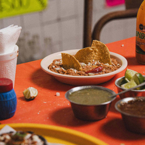 Bowl of refried beans & tortilla chips on an orange table