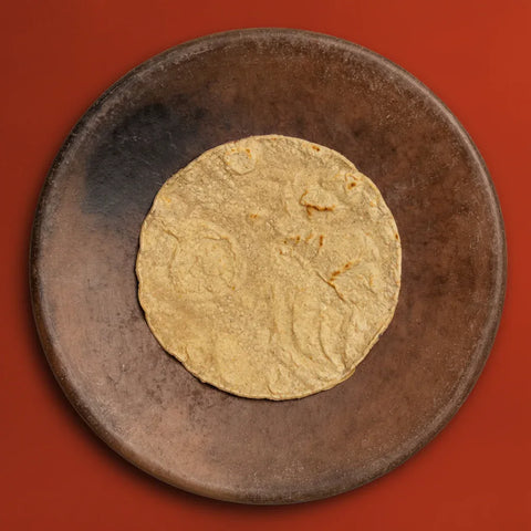Gold tortilla on a dark brown plate against a red background