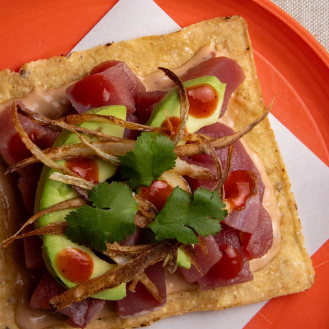 Tostada topped with fish, avocado, and other ingredients on a white plate