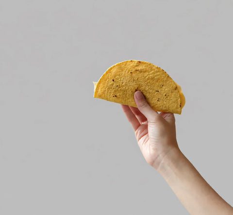 Hand holding a tortilla against a plain background