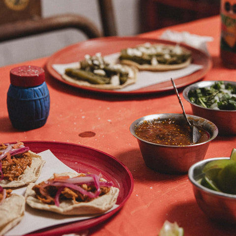 Plates of food on a red table with the focus on a small sauce cup of Taquera salsa