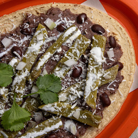 Tortilla with black beans, green chillies, onions, and cheese on an orange plate