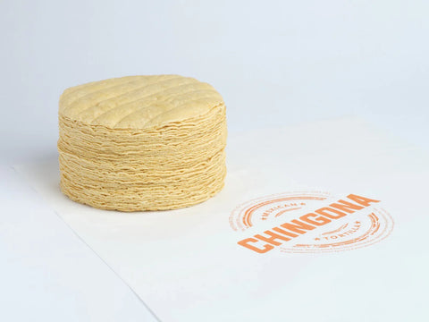 Stack of corn tortillas with a Chingona brand logo on a white background