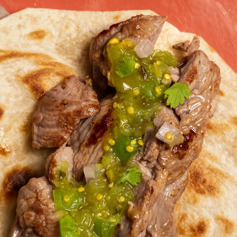 Tortilla with meat and green salsa on a red background