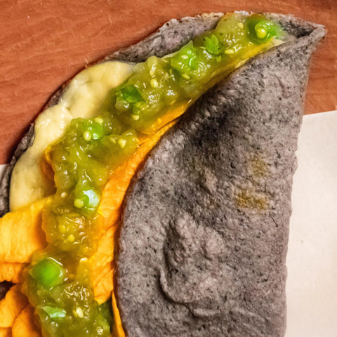 Folded tortilla with cheese and green salsa on a wooden surface