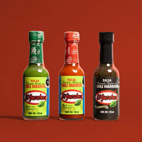Three bottles of El Yucateco hot sauce with colourful labels on a red background