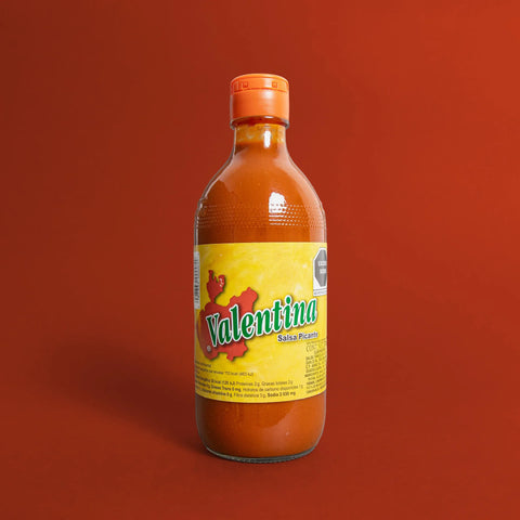 Bottle of Valentina hot sauce (yellow label) on a red background
