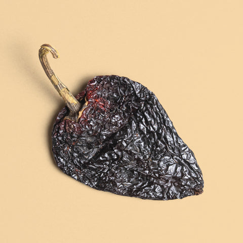 A Single dried ancho pepper on a beige background