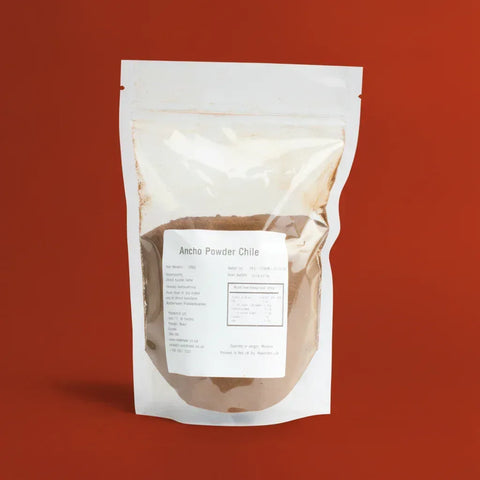A clear plastic food bag with Ancho Powder inside on a red background.
