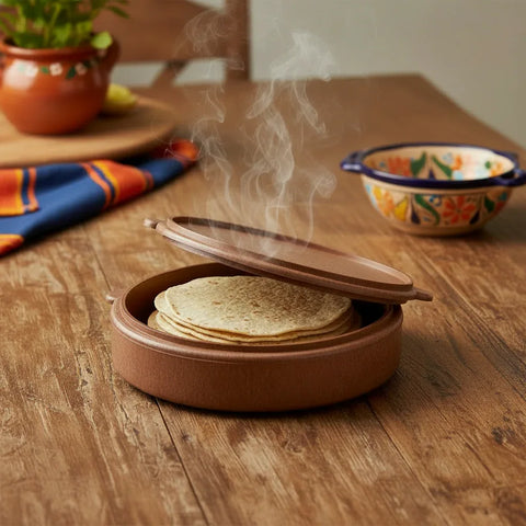Brown tortilla warmer on a wooden table with fresh corn tortillas inside