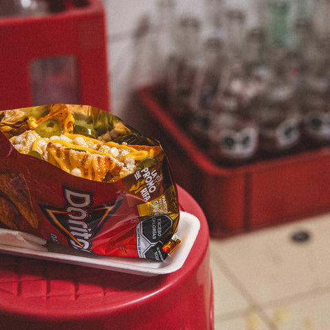 Open bag of Doritos with cheese sauce and jalapenos inside on a red stool with blurred background