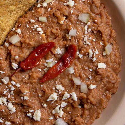 Refried beans dish with chipotle peppers and crumbled cheese on a beige plate.
