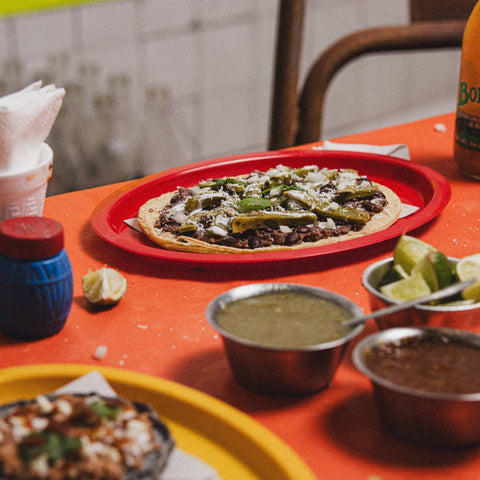 Taco on a red plate with refried beans and jalapenos on an orange table.