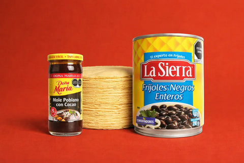 Jar of mole sauce and can of La Sierra frijoles negros enteros and 1kg of fresh corn tortillas on a red background
