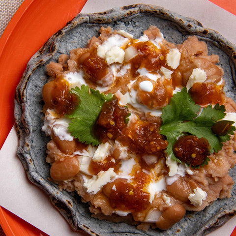 Blue tortilla with refried pinto beans, cheese and Taqera Salsa on an orange plate.