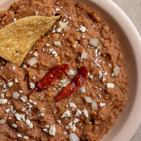 Refried pinto beans dish with tortilla chips and red peppers on a beige plate