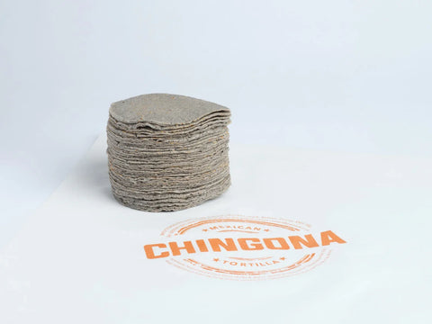 Stack of blue corn tortillas with 'Chingona' branding paper underneath on a white background