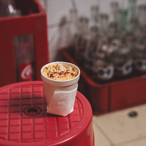 Cup of macaroni and cheese on a red surface with blurred bottles in the background