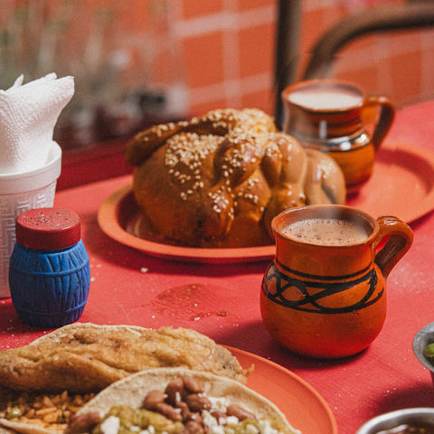 Traditional Mexican food and a hot chocolate drink on a red tablecloth with tortillas, coffee, and a bread roll.