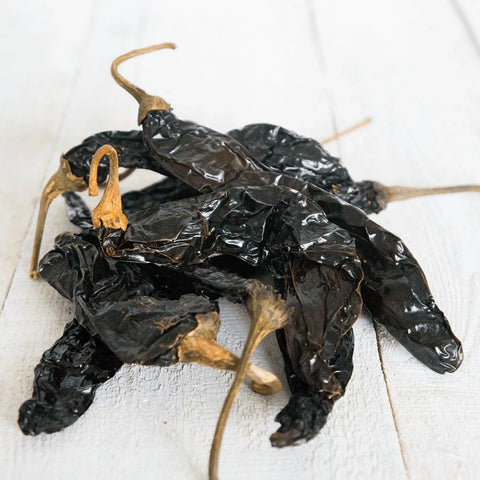 Small pile of dried pasilla chiles on a white wooden background