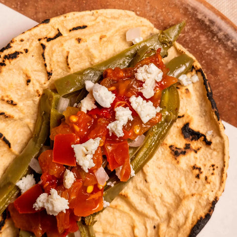 Tortilla with green peppers, red salsa, and white cheese on a wooden surface