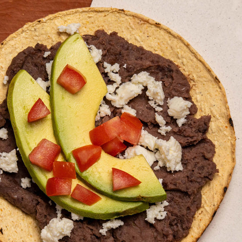 Tortilla with refried beans, avocado, and tomatoes on a wooden surface